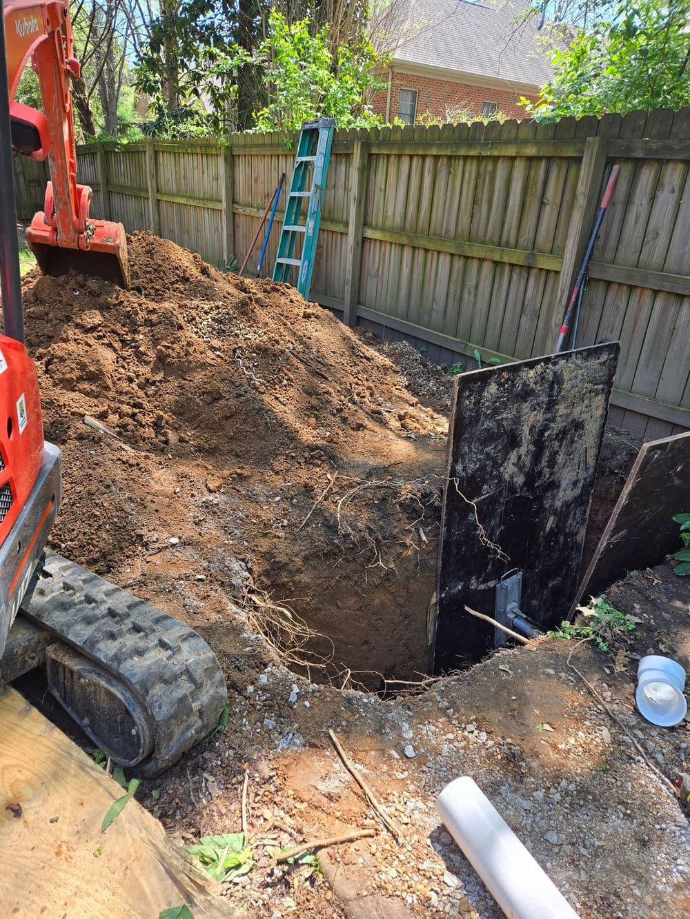 Excavation site with dirt pile and heavy machinery, revealing a large hole in the ground.