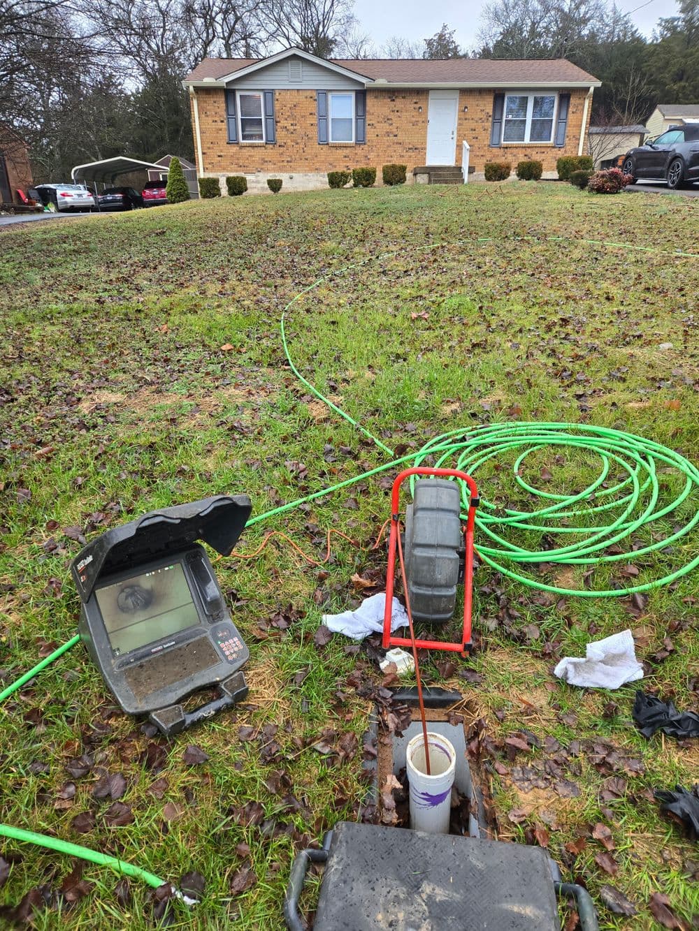 Sewer inspection equipment on lawn with a house in the background and green cables.