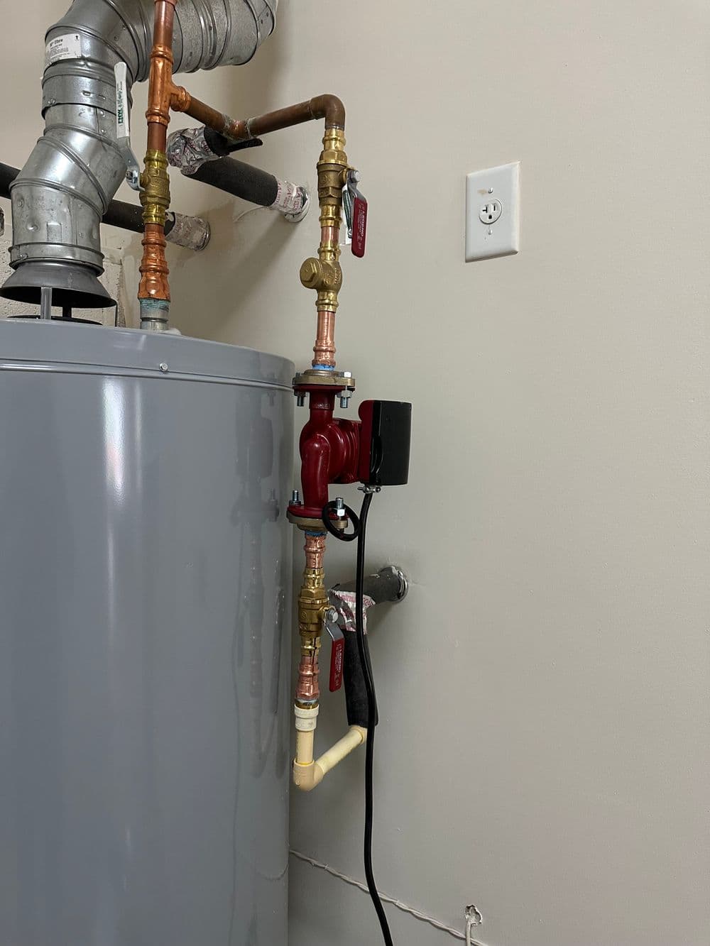 Water heater with copper piping, valves, and electrical connection in a utility room.