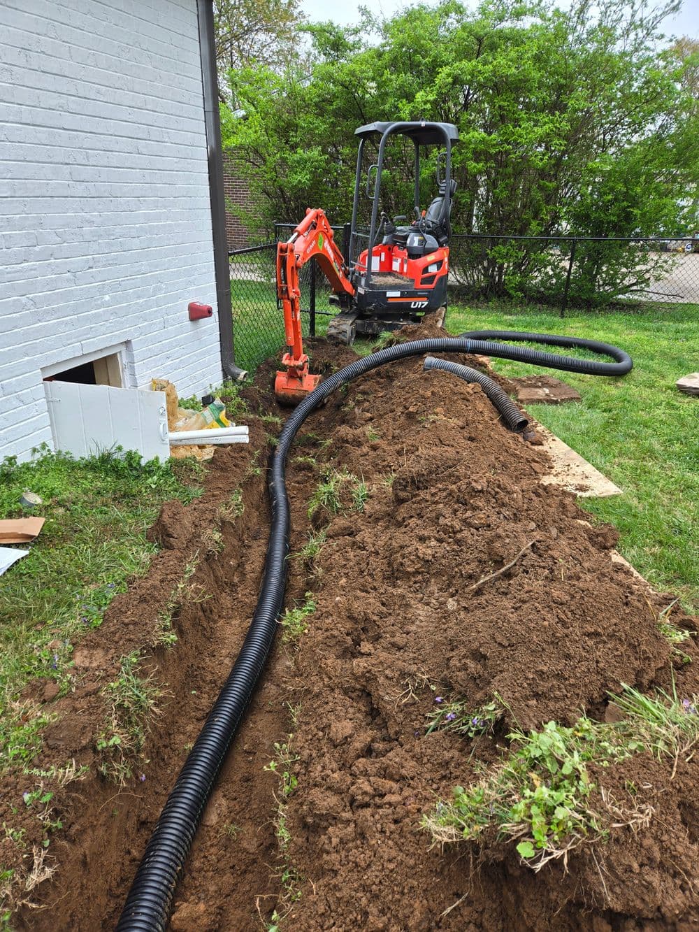 Excavation project with a mini excavator and drainage pipe installation in a backyard.