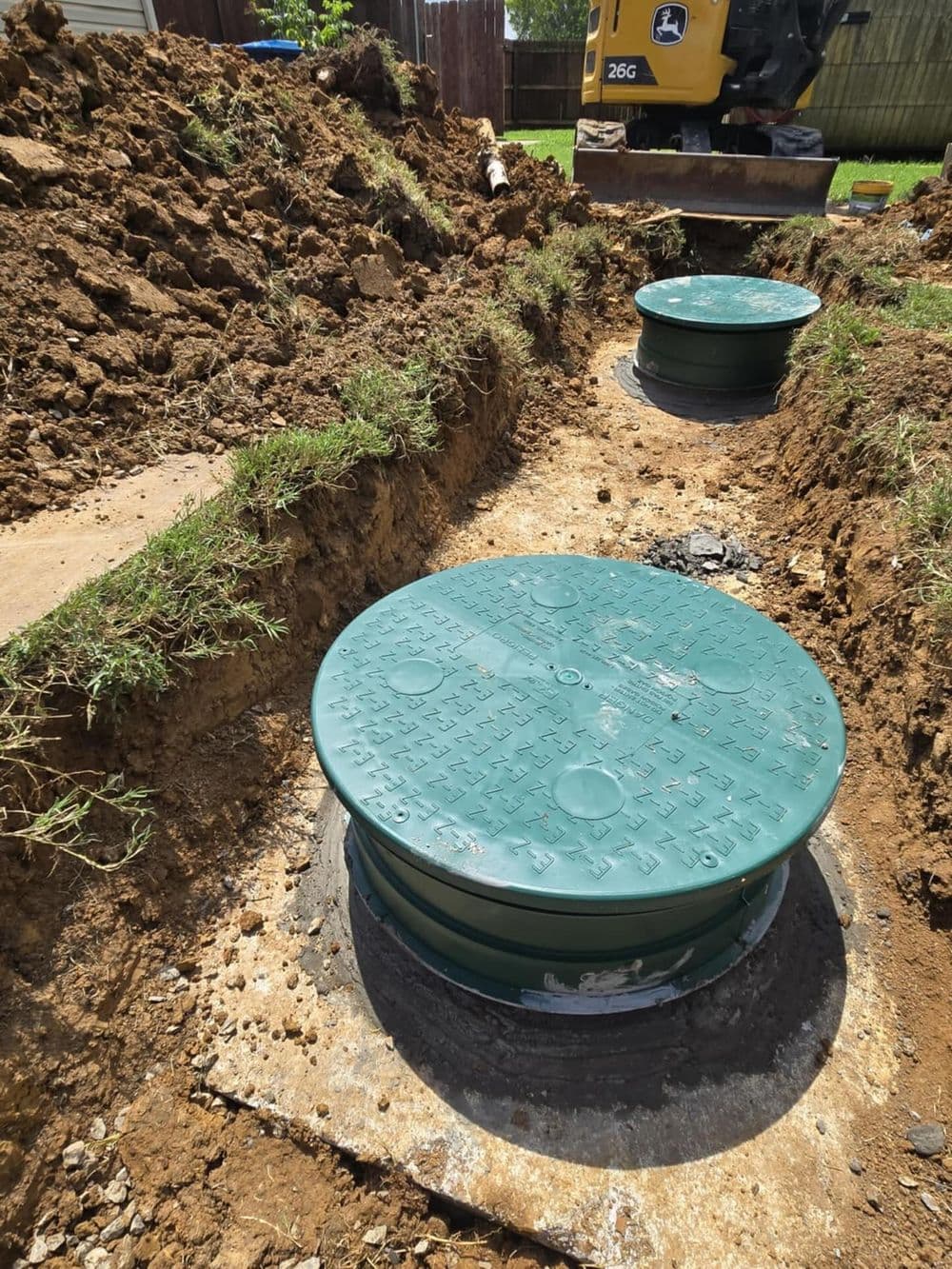 Green manholes installed in a newly excavated area, with machinery in the background.