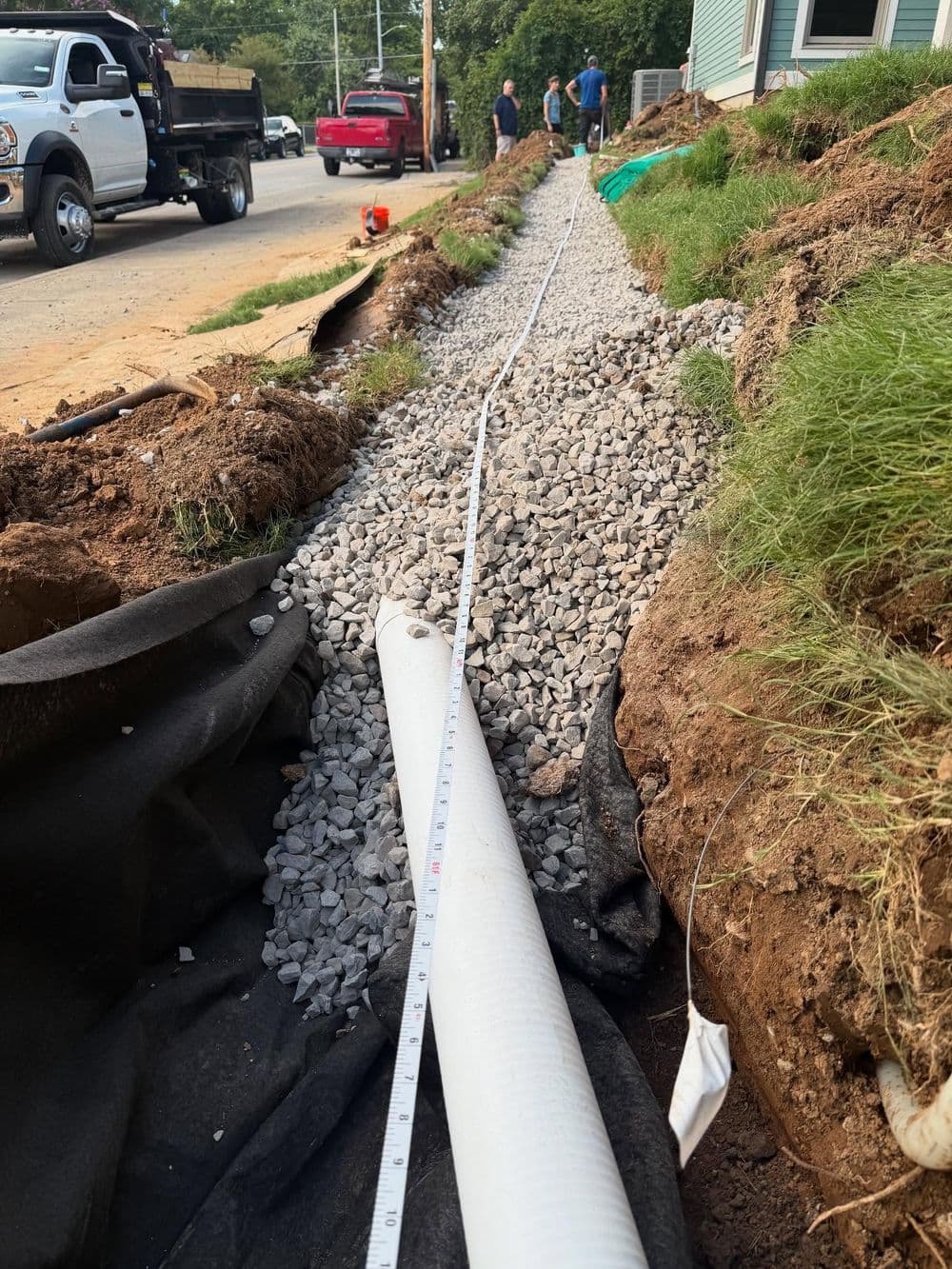 Gravel path installation with drainage pipe alongside road construction site.