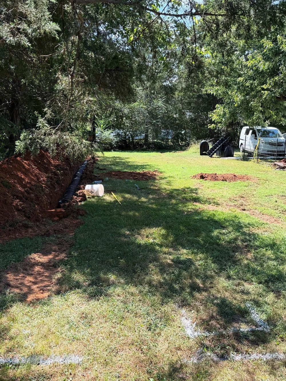 Excavated yard with trenches, grass, trees, and a pickup truck in the background.