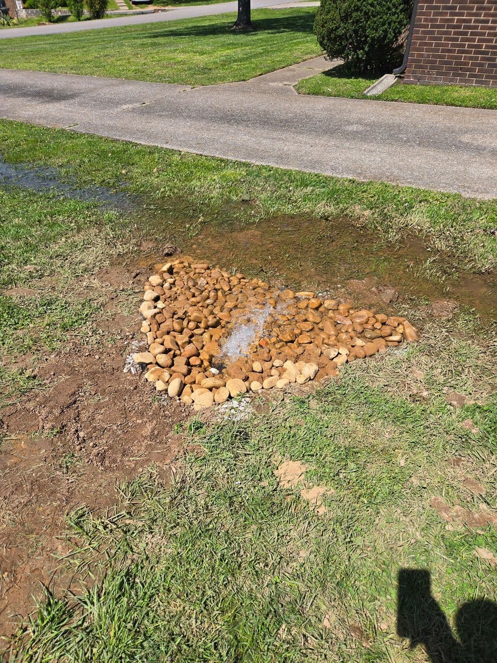 Water flowing over a decorative pebble area in a grassy yard.