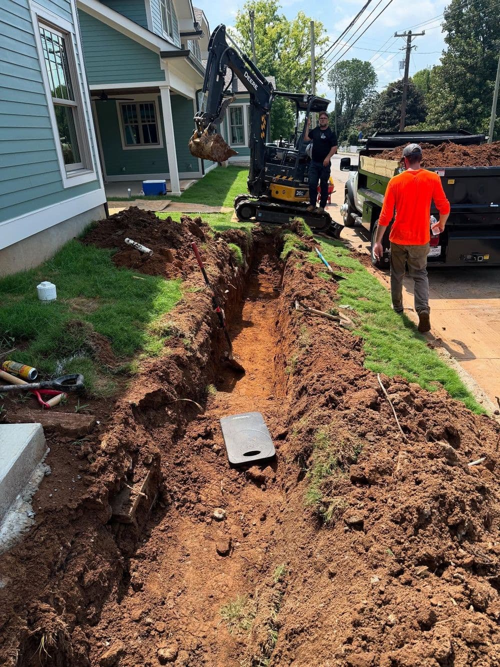 Construction workers digging a trench for utility installation beside a residential building.