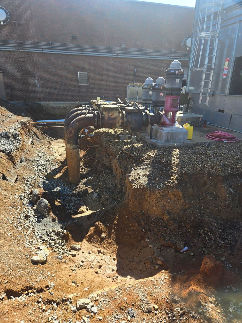 Heavy-duty industrial pipeline with valves buried in excavated ground near a building.