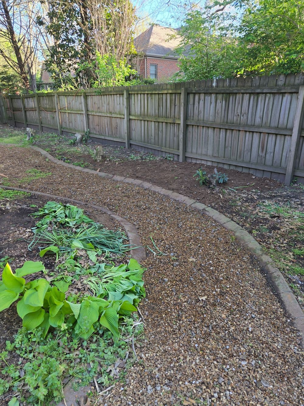 Garden path with gravel winding through a landscaped yard and lush green plants.